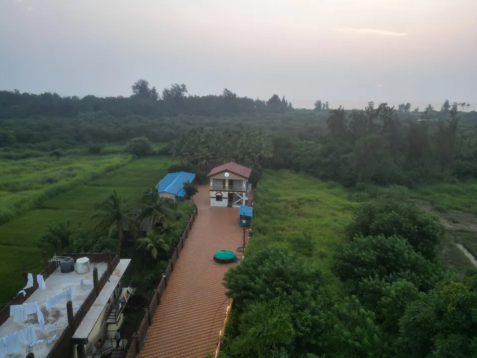 Aerial view of the villa and its tiled path, with green fields and trees around and a neighbouring building in the foreground