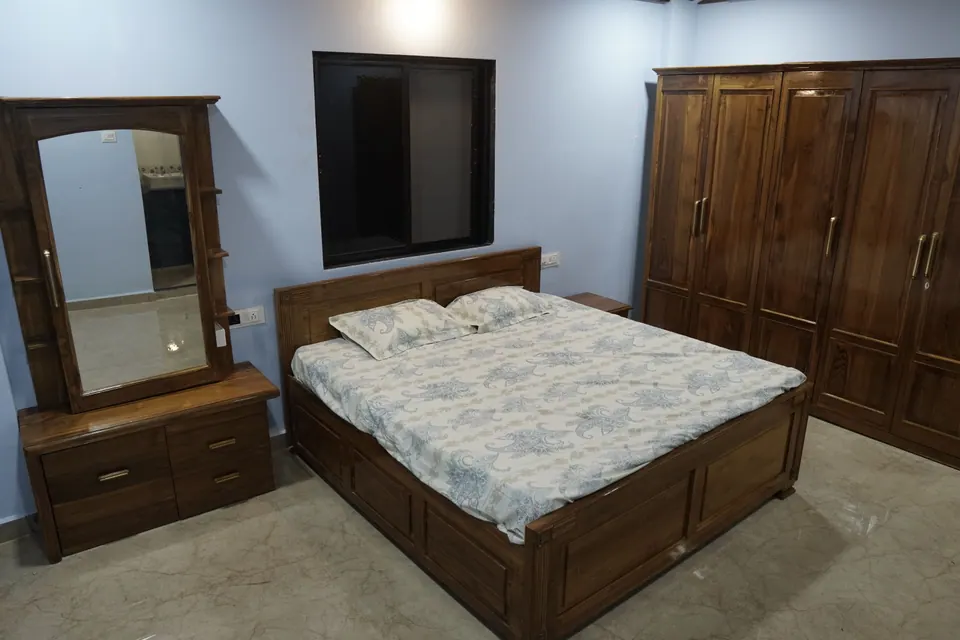 Bedroom with blue walls, a wooden bed, a mirrored dressing table and a large wooden wardrobe