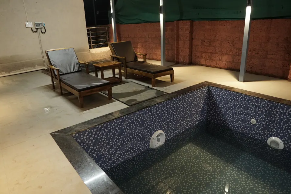 Tiled pool with wooden sun loungers and side tables beside it, on a covered terrace at night
