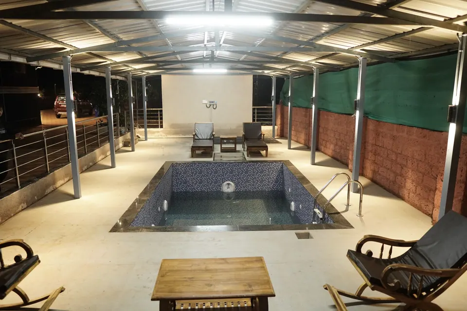 Small tiled pool on a covered terrace with a steel railing, wooden loungers and a table, lit at night