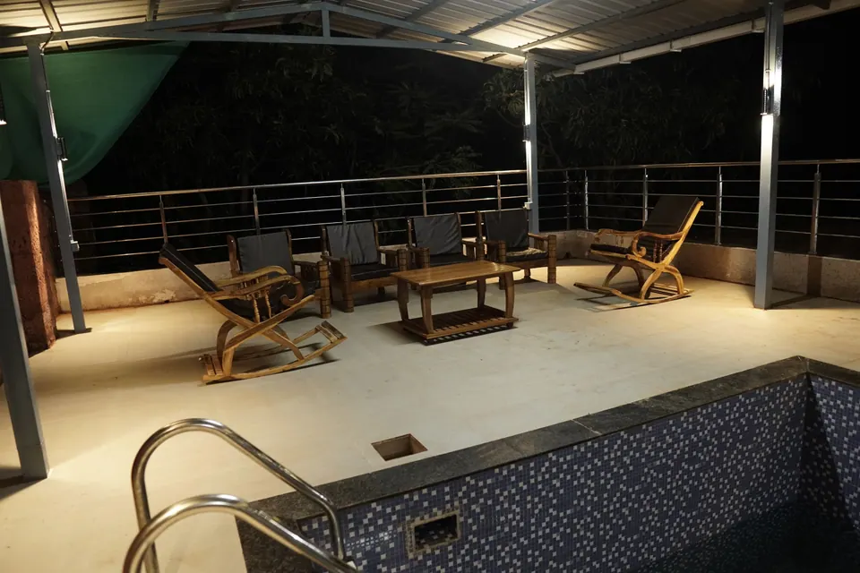 Cane-and-wood chairs and a coffee table on the terrace beside the pool, at night