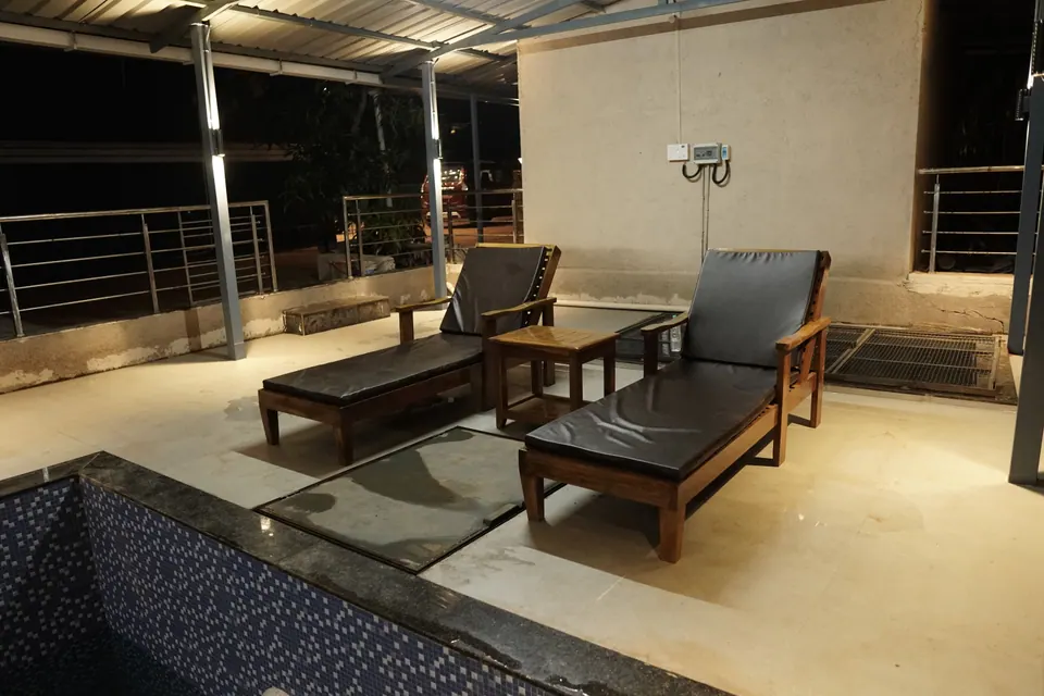 Two wooden sun loungers with a side table next to the edge of the pool, at night