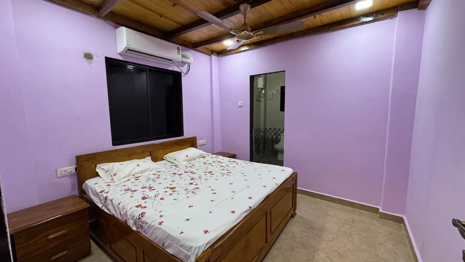 Bedroom with lilac walls, a wooden bed with a floral bedsheet and an air conditioner