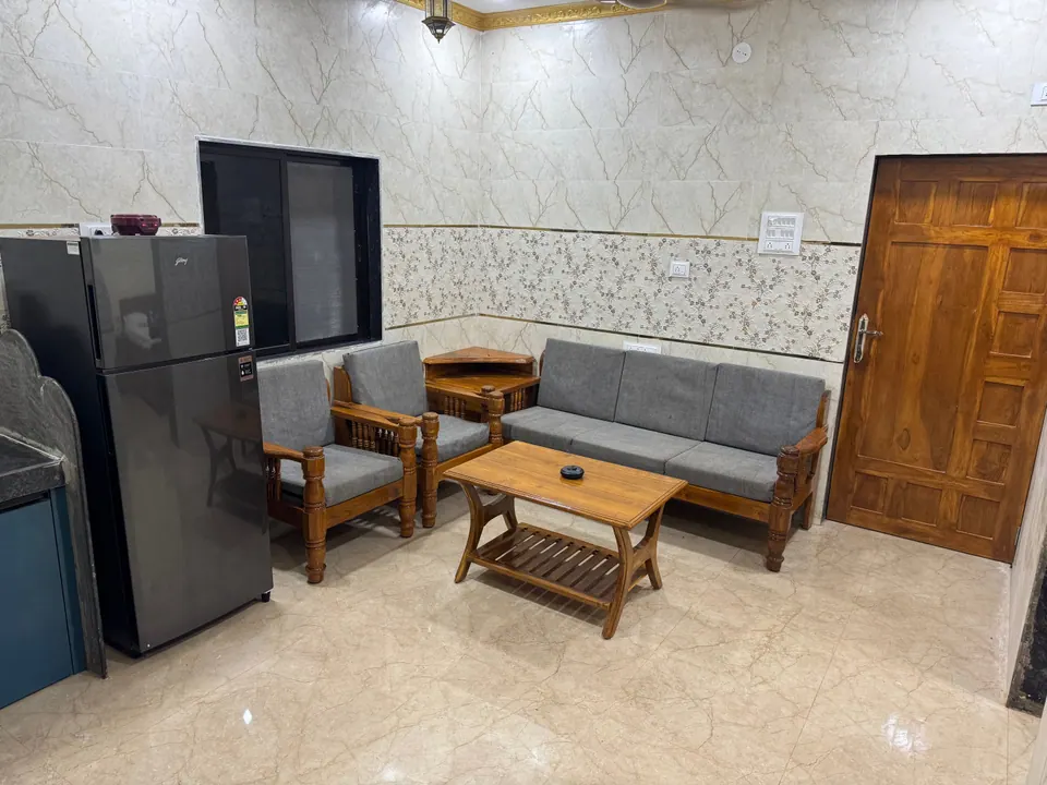 Sitting area with a grey sofa, armchairs and a wooden coffee table, with a refrigerator beside the kitchen counter