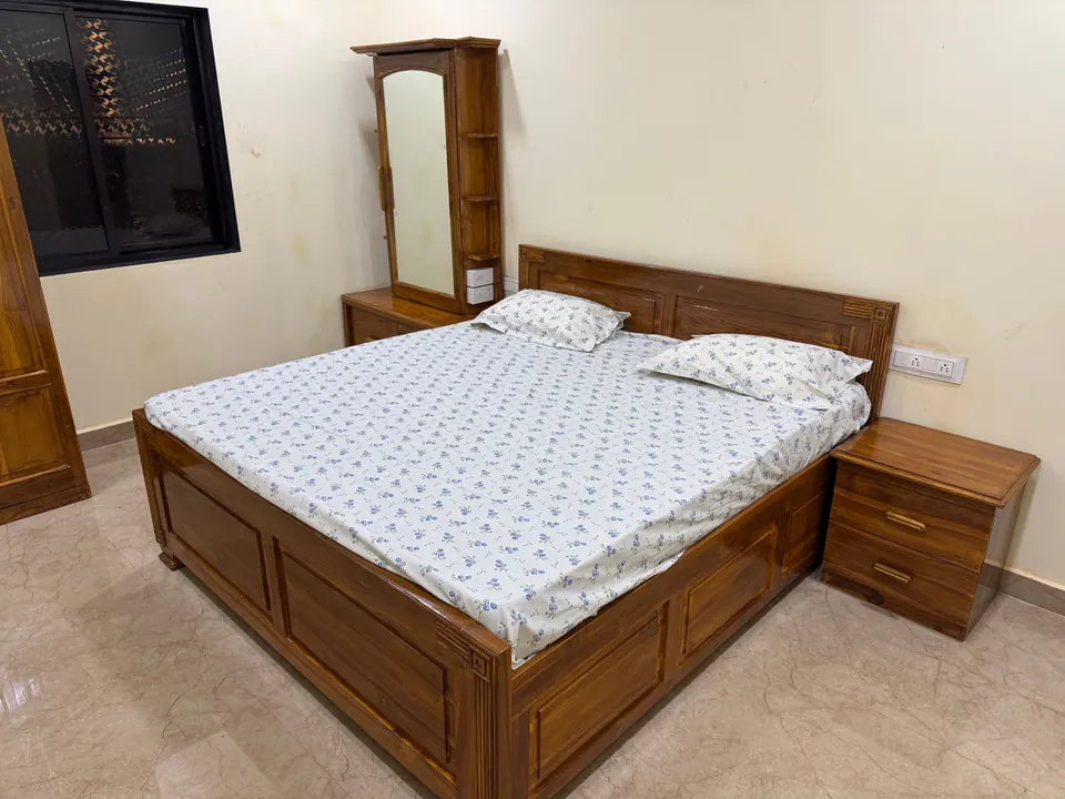 Wooden bed with a patterned bedsheet and a bedside table, next to a dressing table